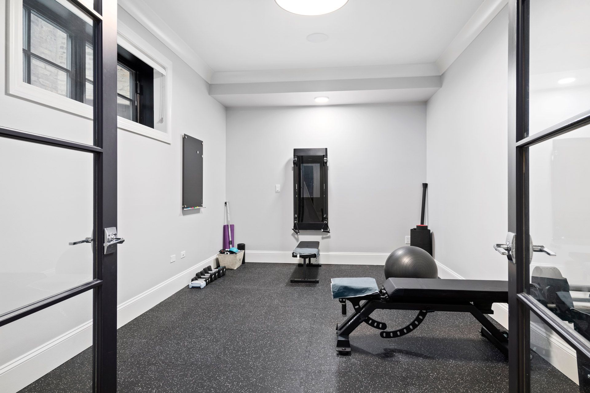 Minimal workout room with black bench, exercise ball, and mirrored wall in a bright white interior