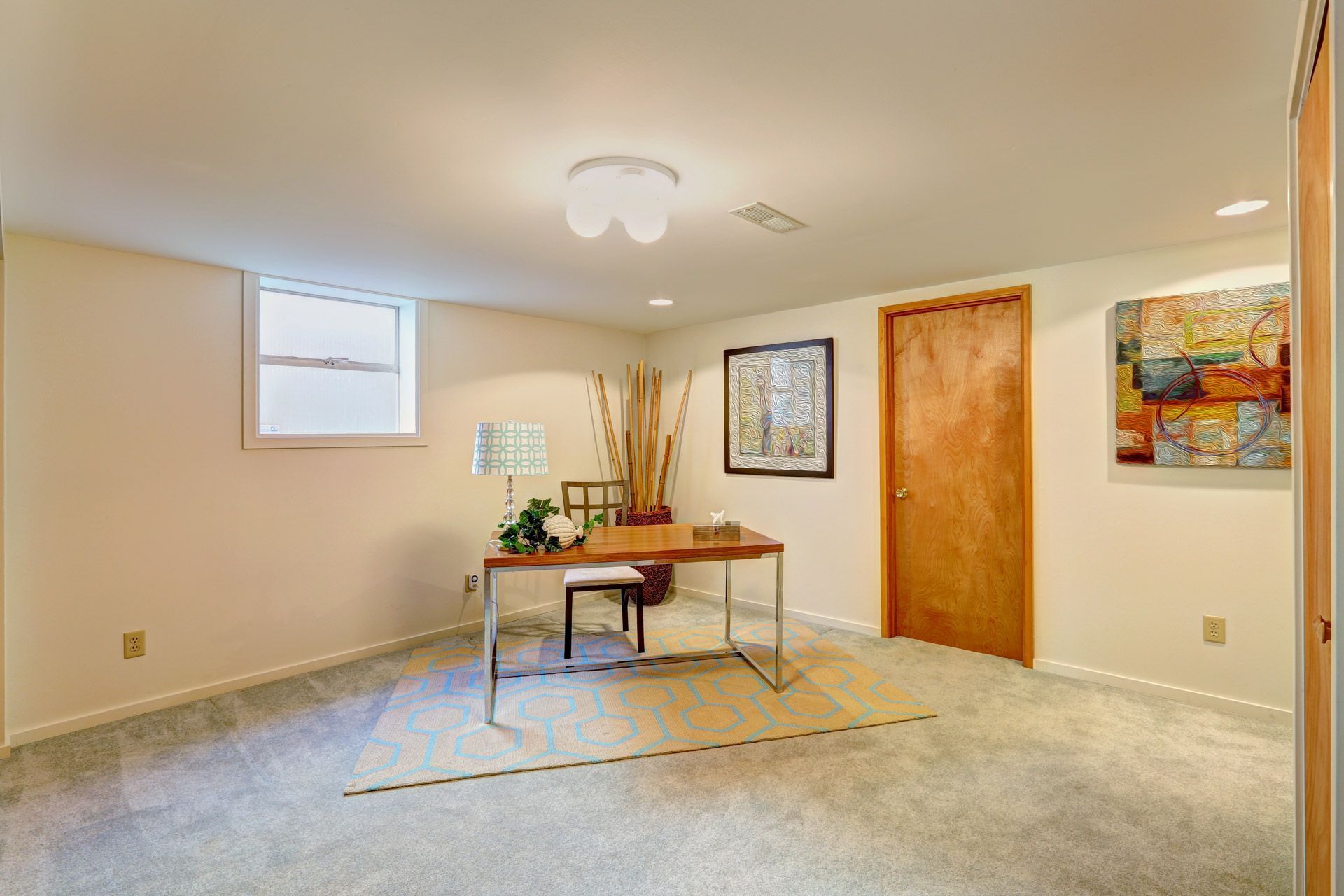Empty carpeted room with a small table, wooden doors, framed wall art, and a ceiling light