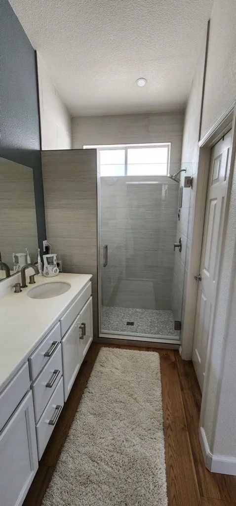 Narrow bathroom with white vanity, shower at the end, and a beige runner rug on the floor