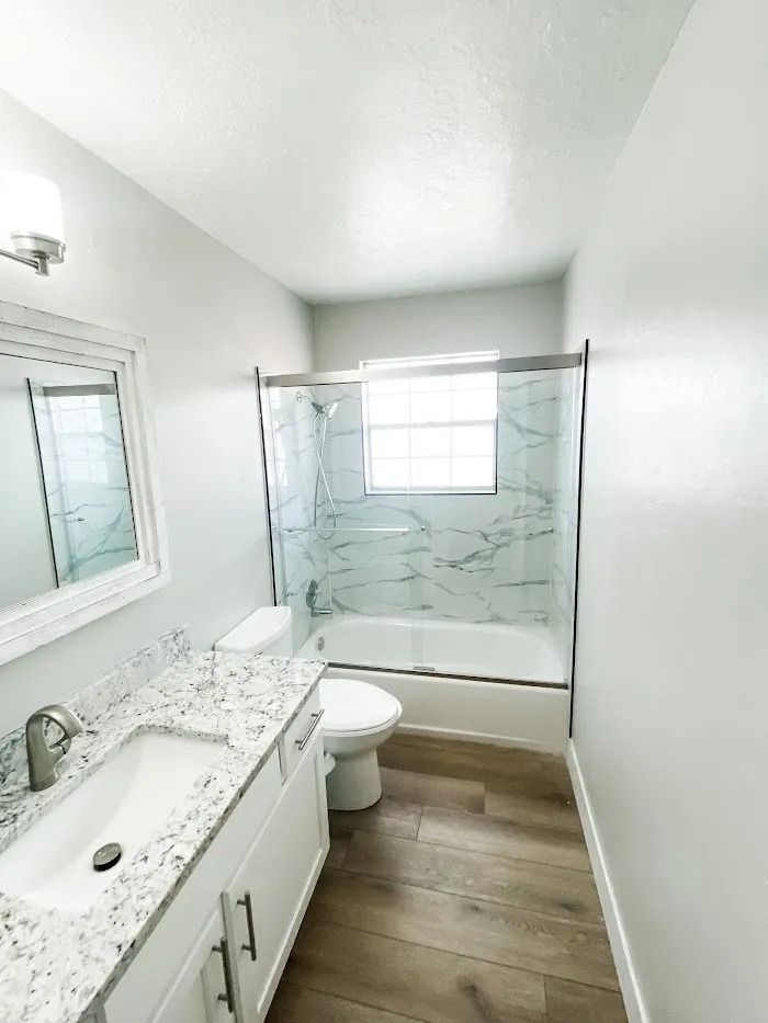 Bright modern bathroom with white vanity, large mirror, glass shower, and wood-look tile floor