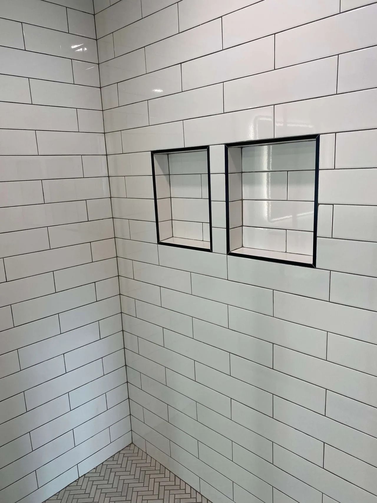 White tiled shower corner with two small built-in soap shelves.