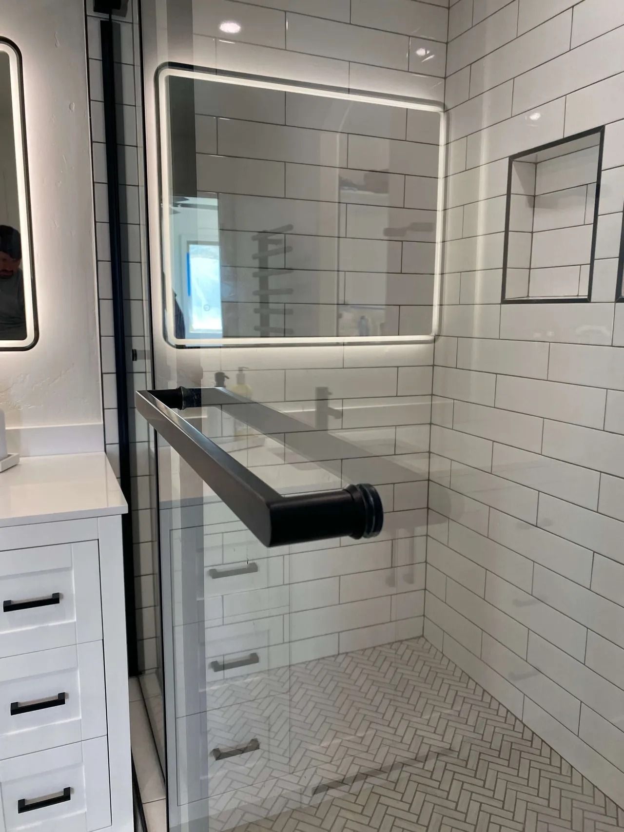 Modern bathroom with white subway tile, illuminated mirror, and black floating vanity shelf