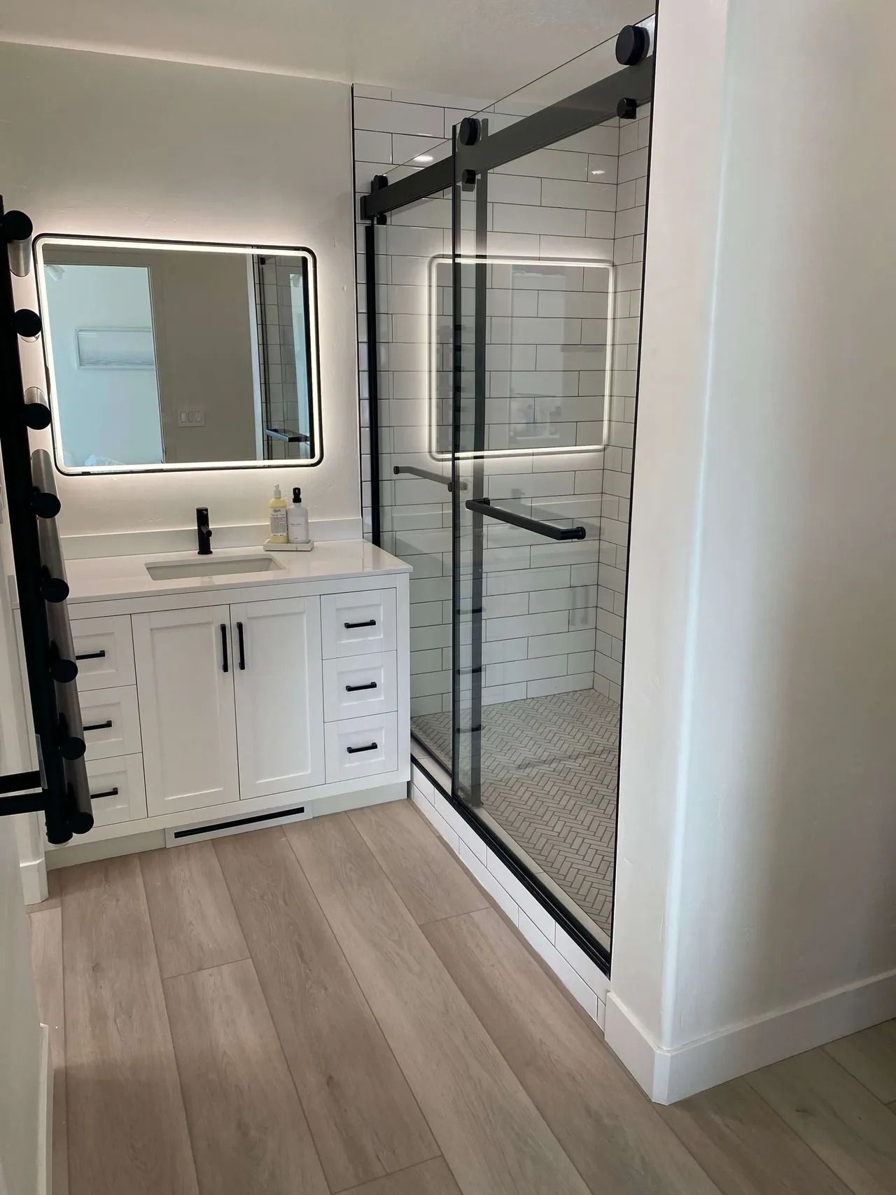 Modern bathroom with glass shower, white vanity, mirror, and light wood flooring