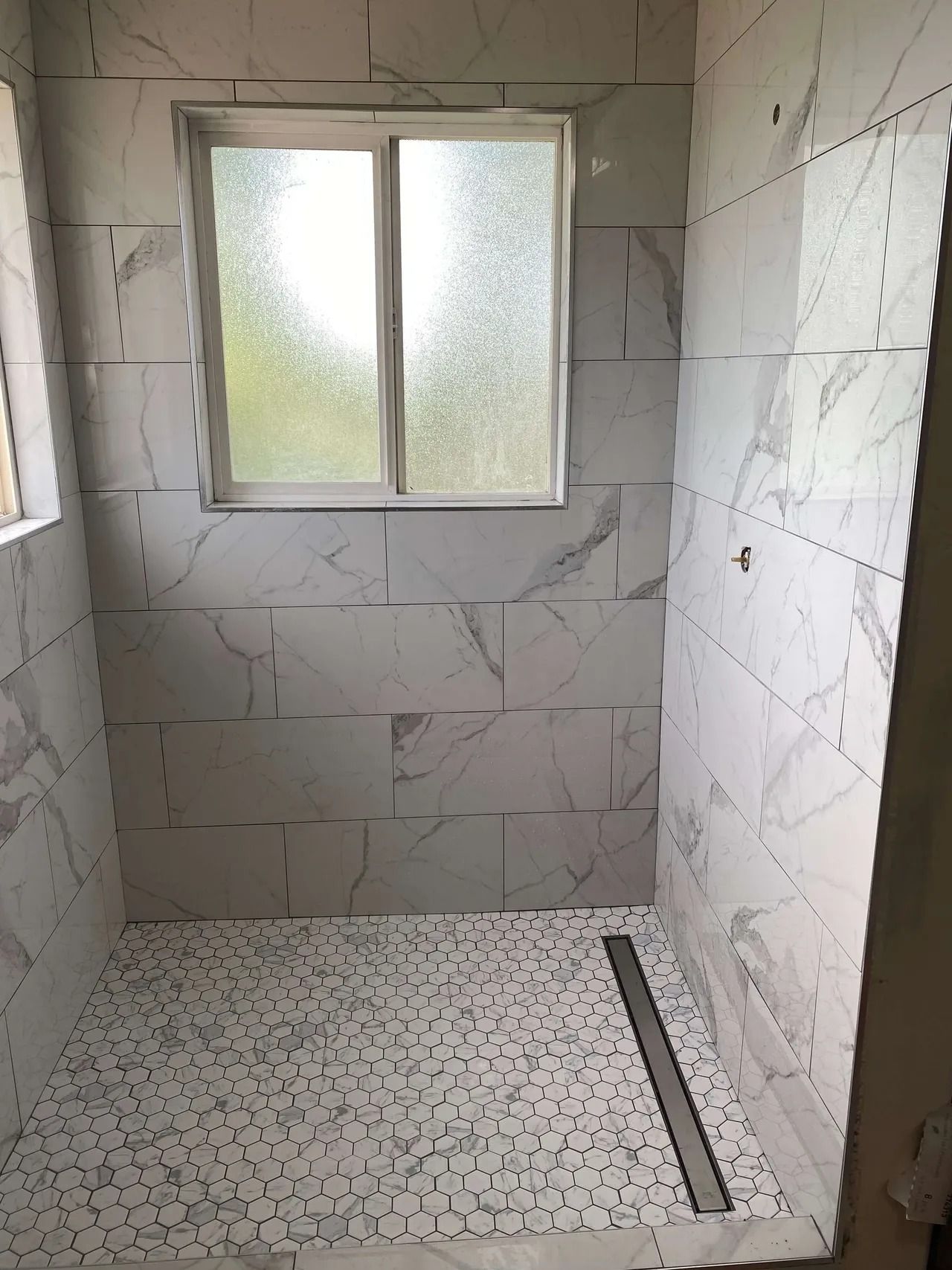 Small tiled bathroom with a frosted window and a shower drain on the floor.