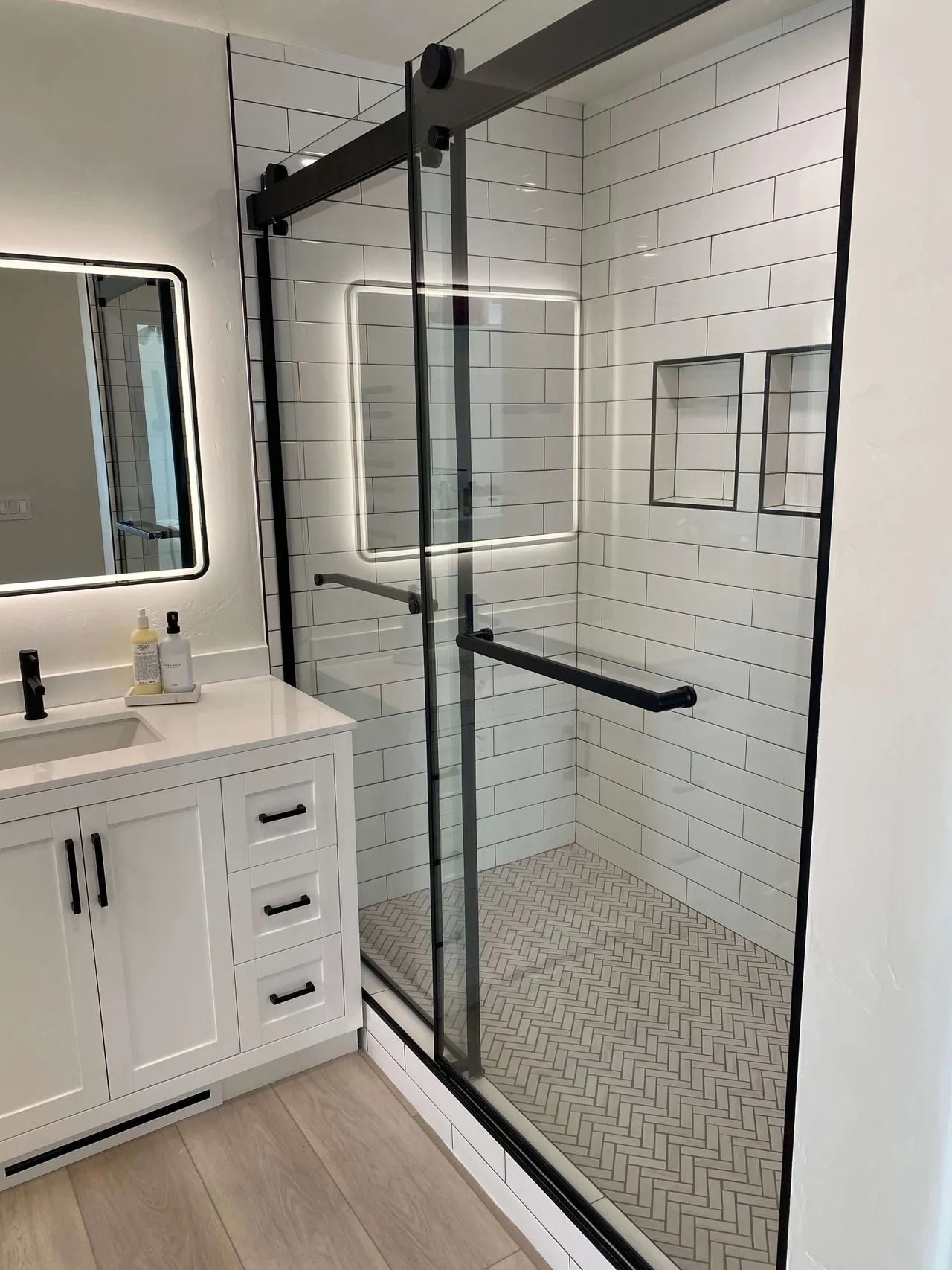 Modern bathroom with white vanity, mirror, and black-framed glass shower enclosure