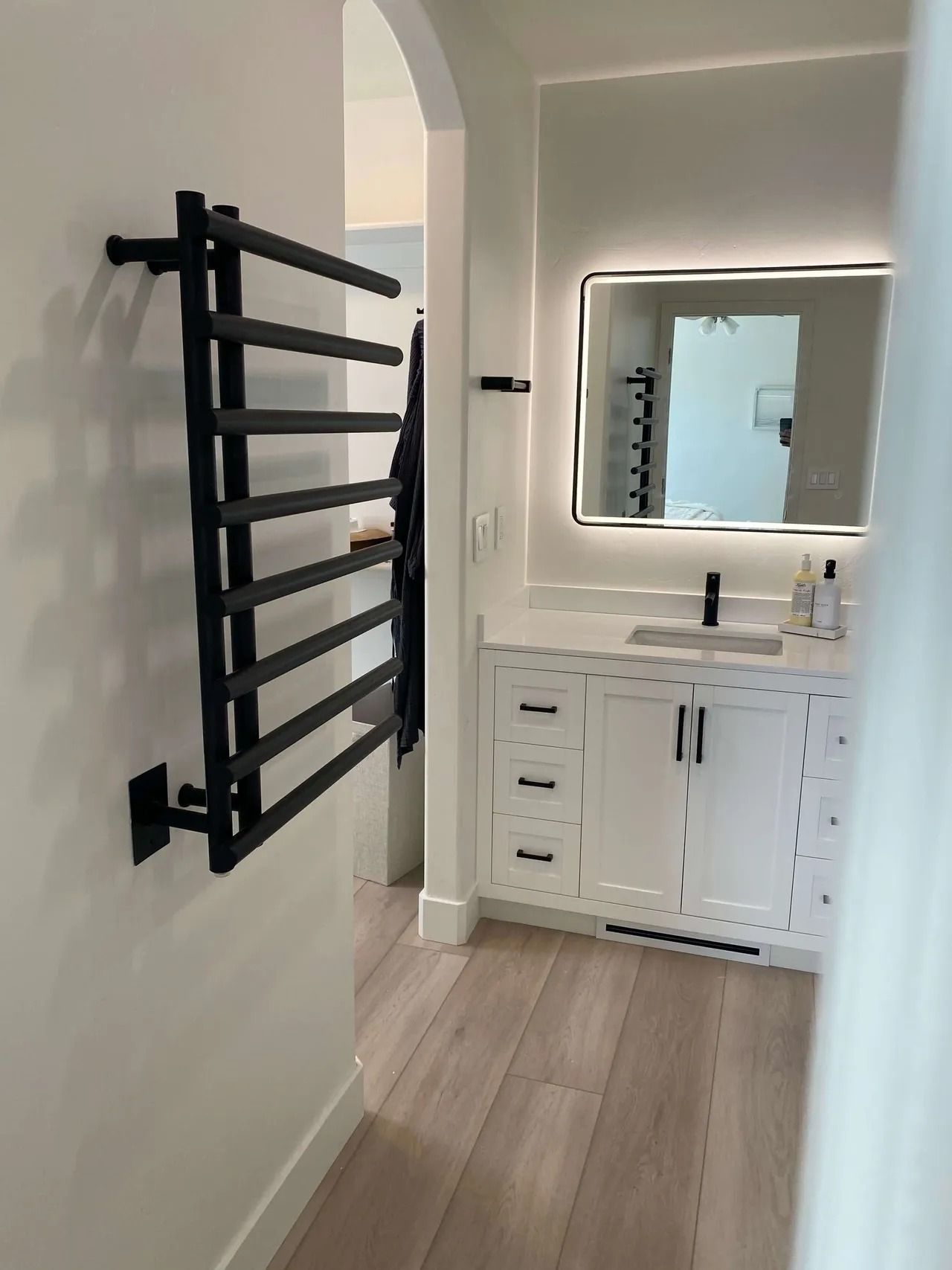 Bathroom with black wall ladder, white vanity, mirror, and light wood floor
