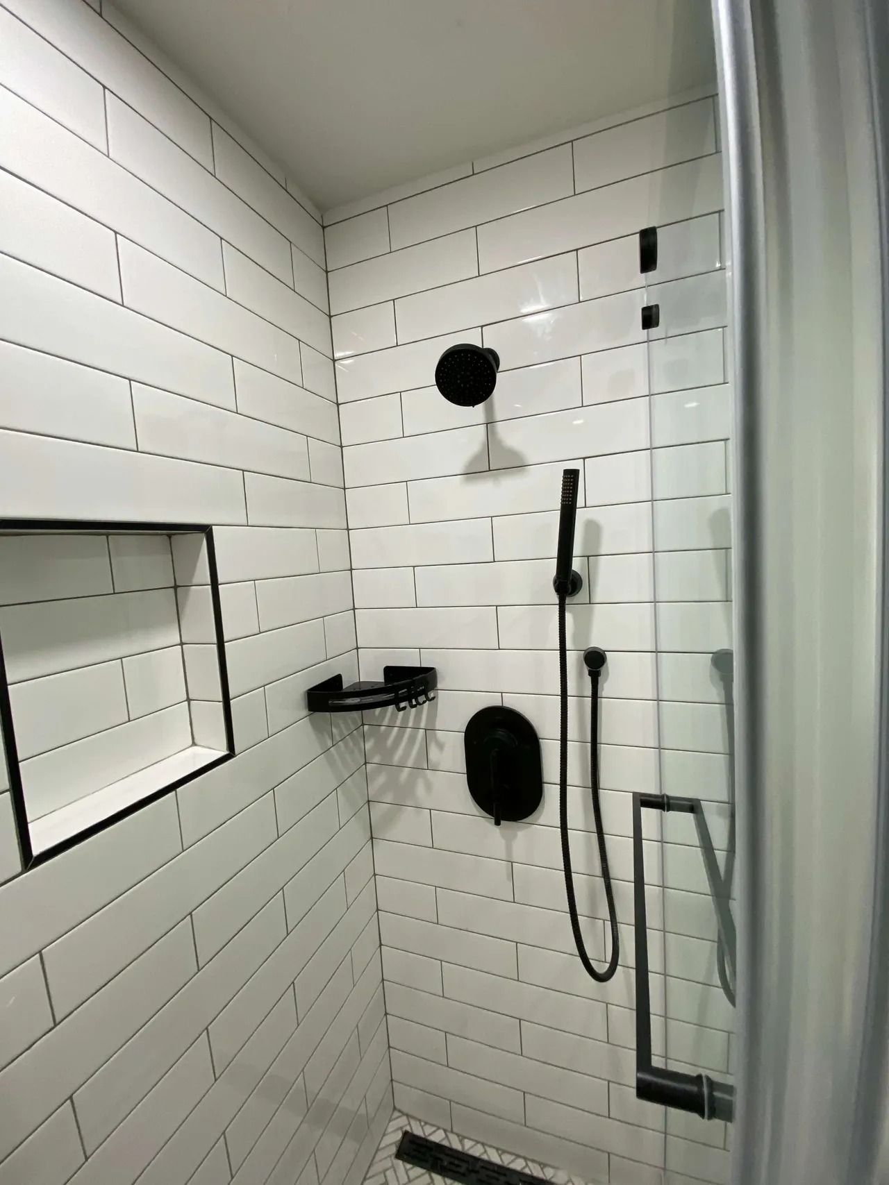 Black-and-white tiled bathroom shower with handheld showerhead, niche shelf, and grab bars