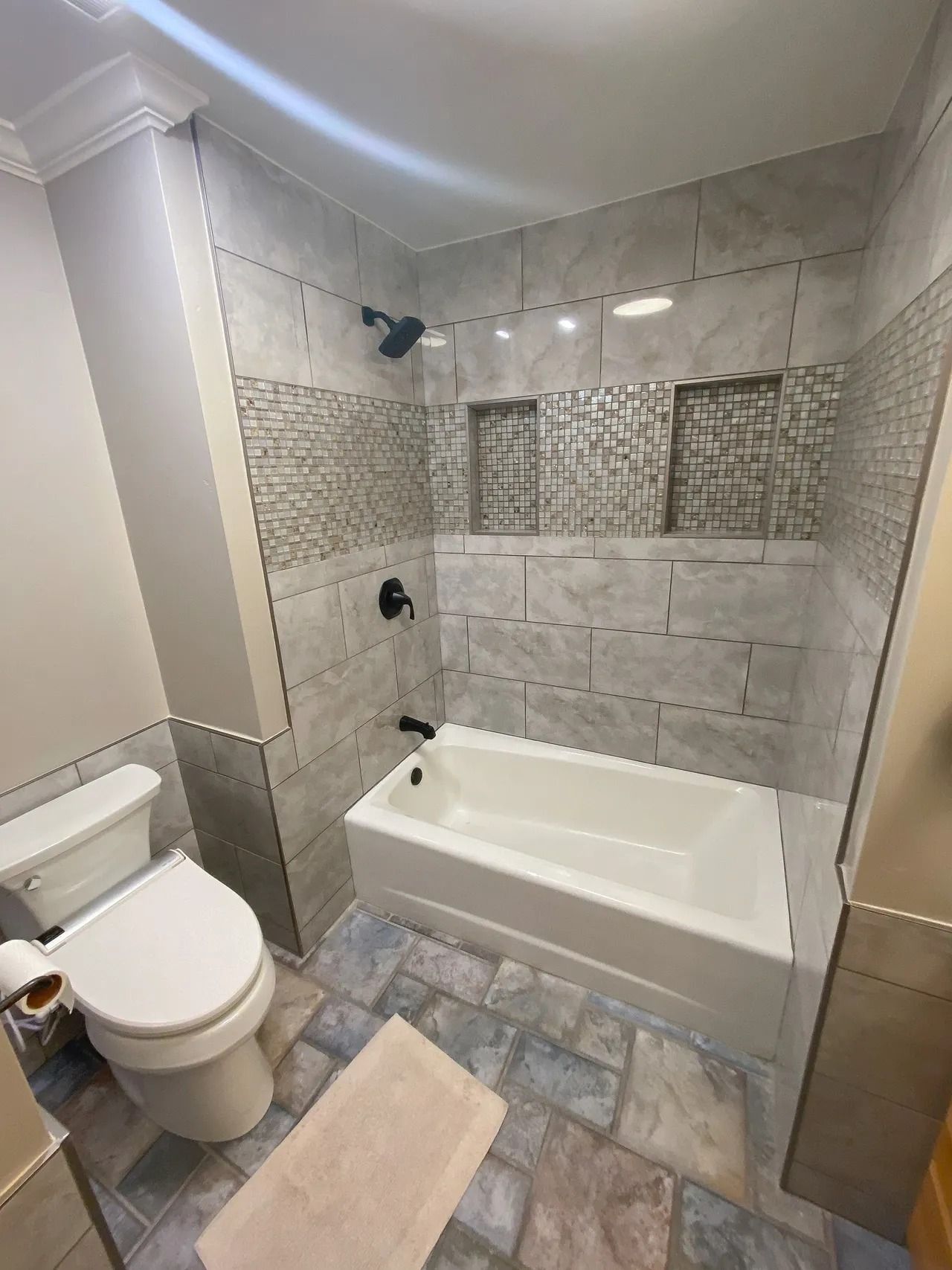 Modern tiled bathroom with a bathtub, toilet, and beige floor tile.