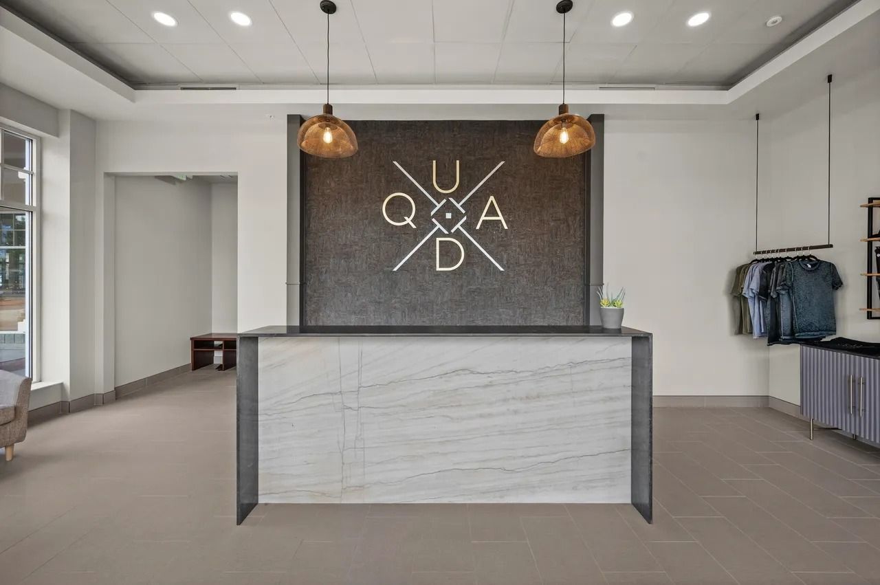 Modern boutique reception desk with white walls, pendant lights, and a clothing rack in a minimalist lobby.