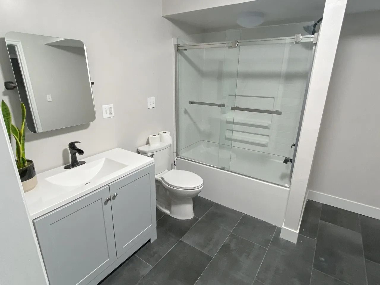 Modern white bathroom with vanity, toilet, glass shower, and dark gray tile floor.
