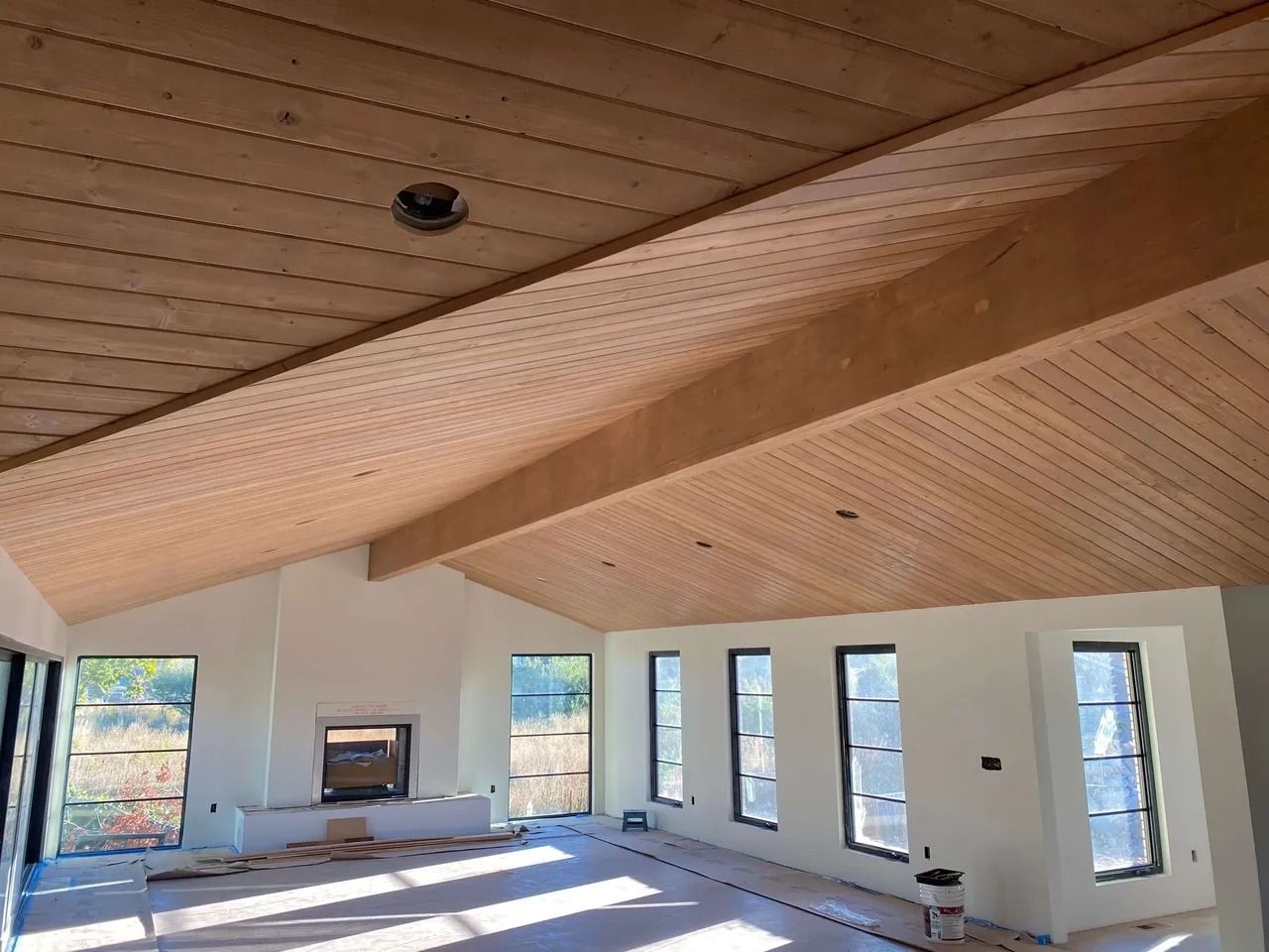 Empty modern room with sloped wood ceiling, white walls, and tall windows overlooking trees