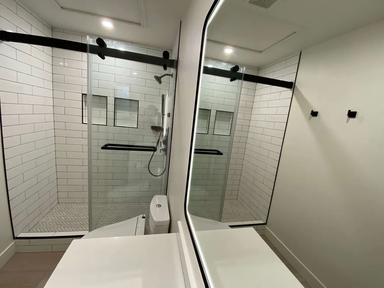 Modern bathroom with glass shower, white subway tile, and large mirror above a sink.