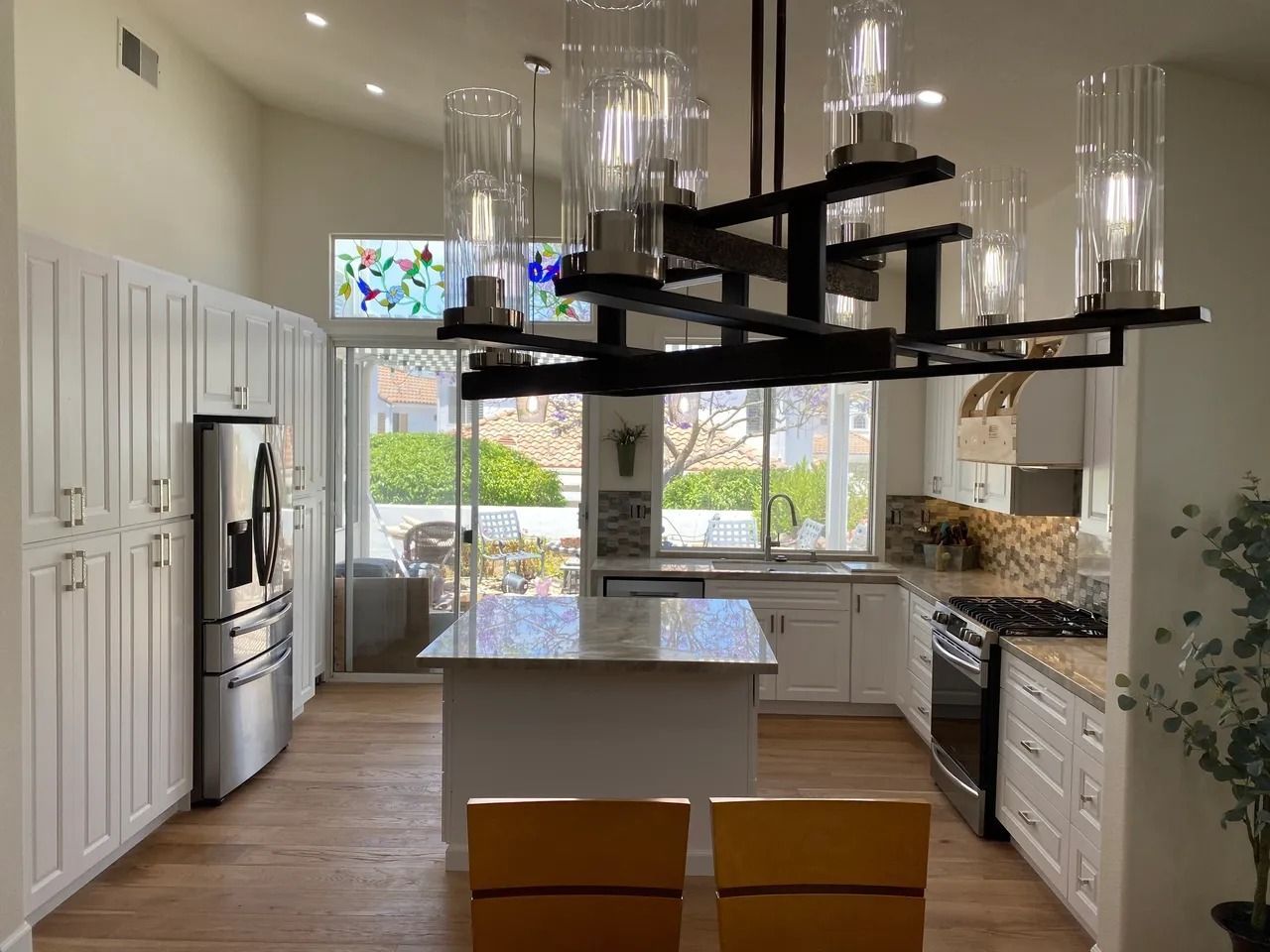 Modern white kitchen with island, black hanging pot rack, stainless appliances, and wood flooring