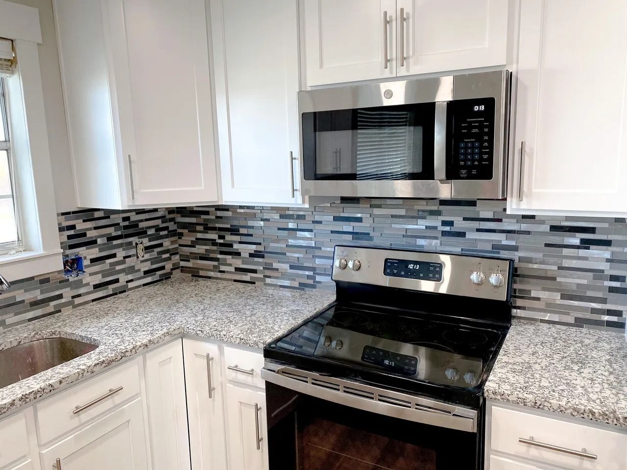 Modern kitchen with white cabinets, granite counters, mosaic backsplash, and stainless steel microwave and stove.