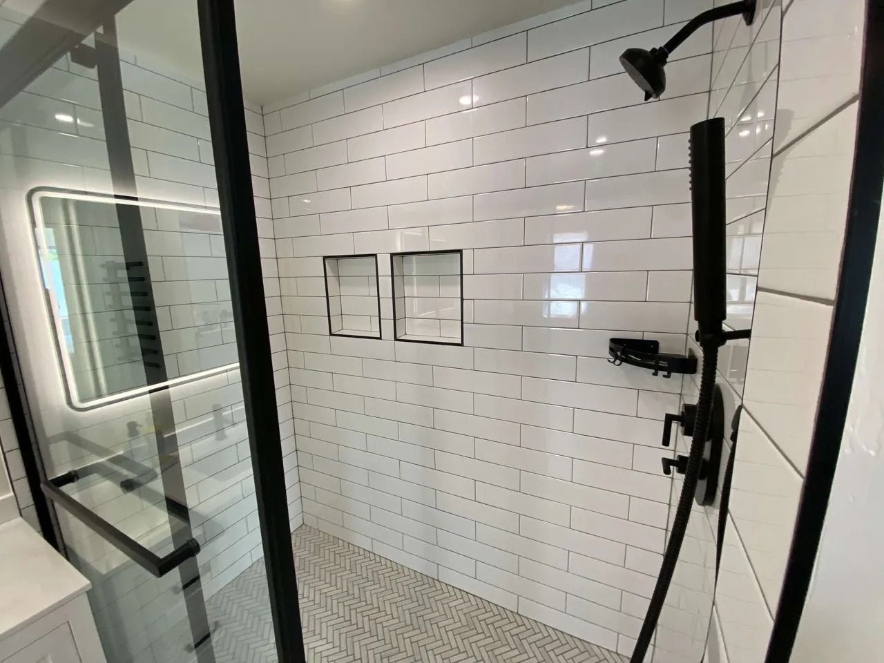 Modern bathroom shower with glass door, white subway tile, and black fixtures