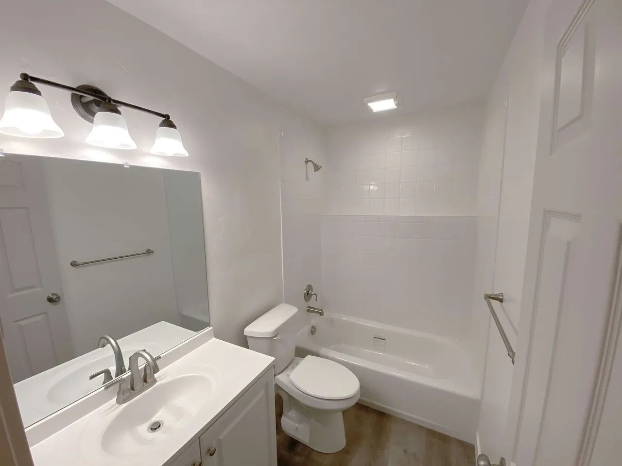Bright white bathroom with vanity, toilet, bathtub, and mirror lights