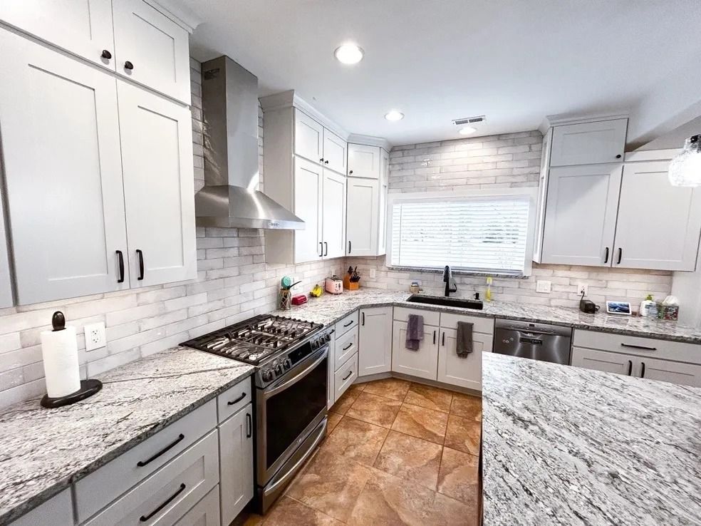 Bright white kitchen with gray cabinets, marble counters, stainless stove, and wood-look floor