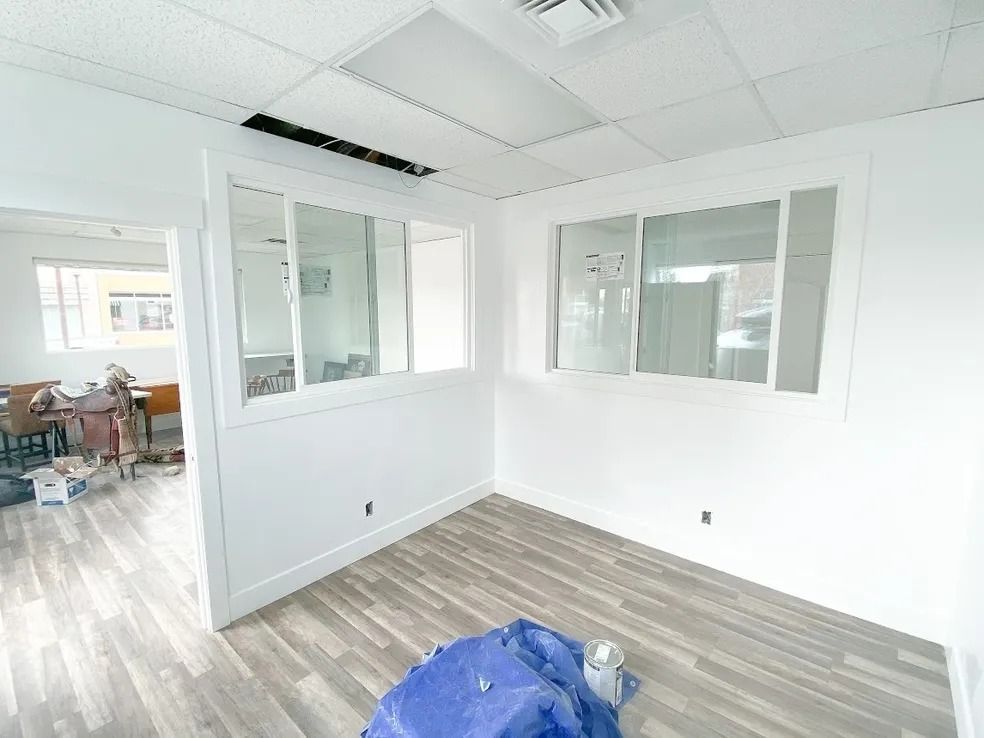 Empty office room with white walls, glass partitions, and wood-look flooring under renovation