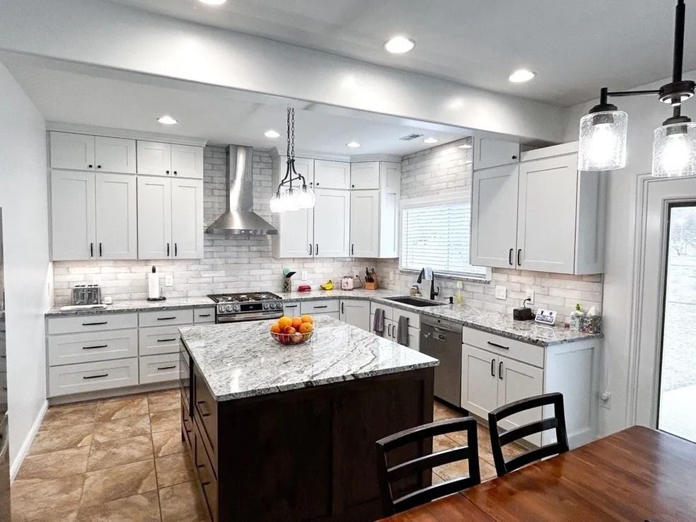 Bright modern white kitchen with gray cabinets, marble island, stainless appliances, and dining table