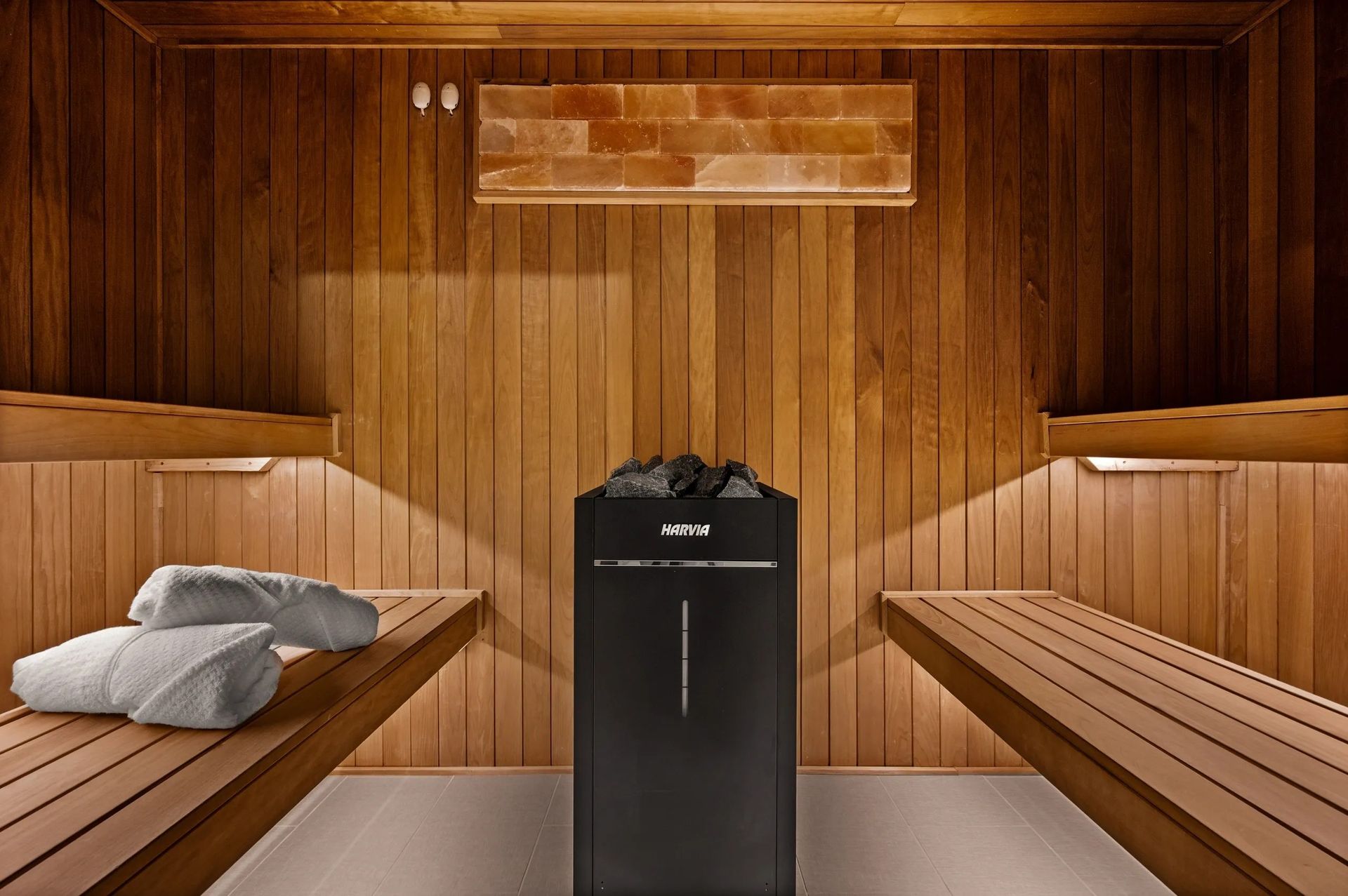 Wood-paneled sauna with wooden benches and a black heater in the center
