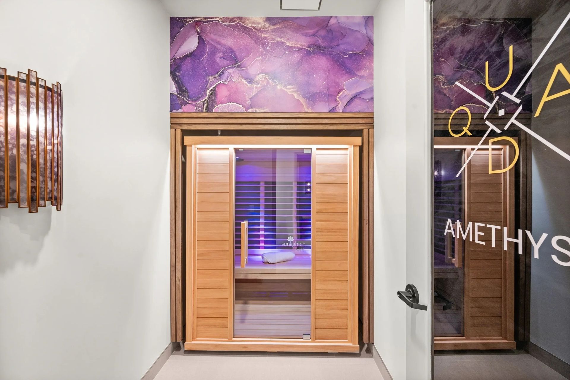 Spa entrance with a wooden sauna door, purple mural above, and dim neon signage to the right