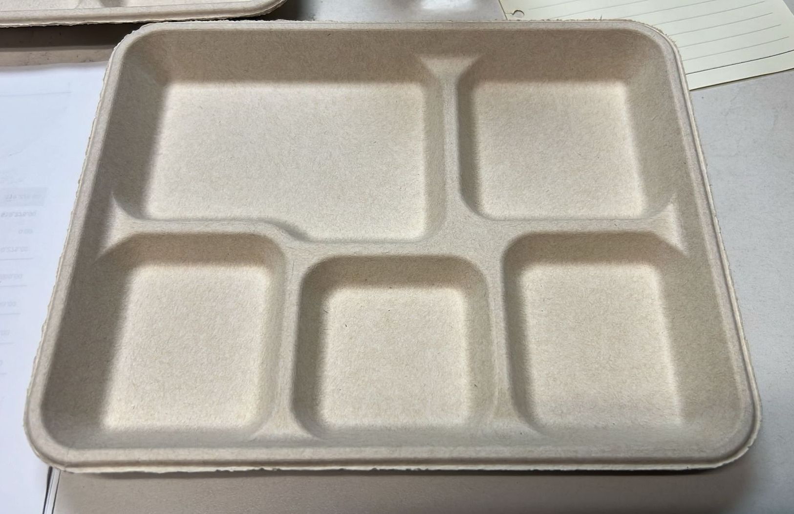 A beige, divided disposable food tray with five compartments, viewed from above.