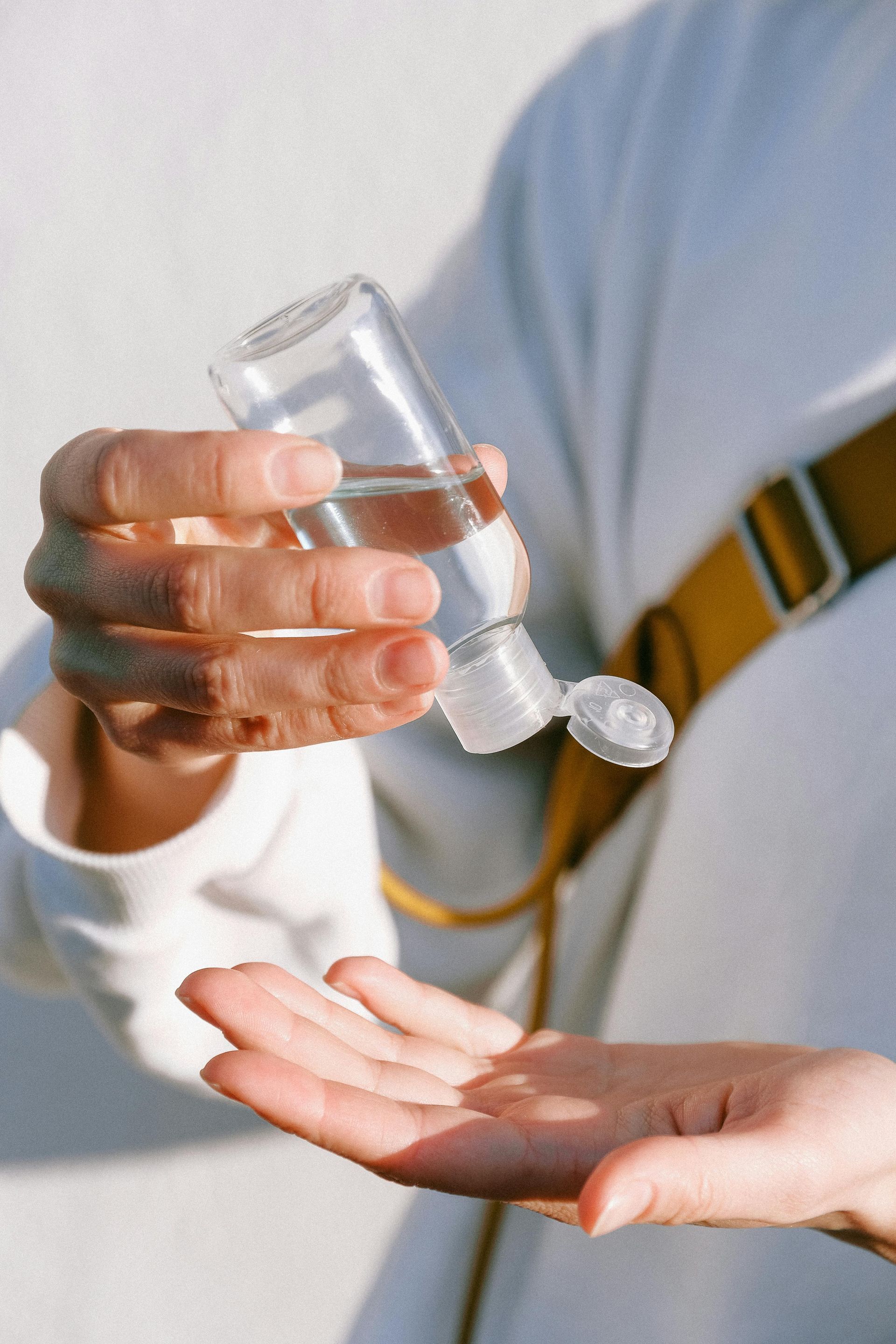 Person pouring hand sanitizer from a clear bottle into their palm.