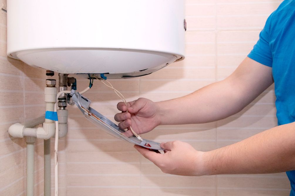 Una persona stringe un tubo dello scaldabagno con una chiave inglese in un bagno piastrellato.