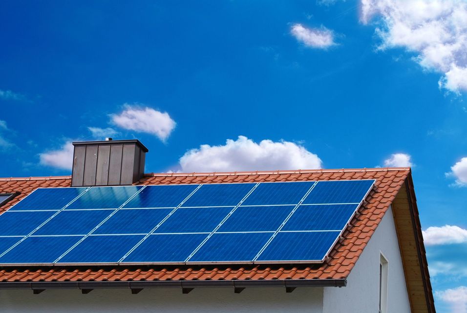 Pannelli solari sul tetto di una casa sotto un cielo azzurro brillante con nuvole
