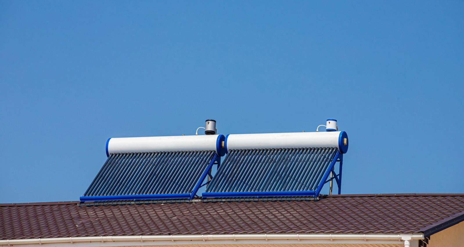 Pannelli solari per il riscaldamento dell'acqua installati sul tetto di una casa, sotto un cielo azzurro e limpido.