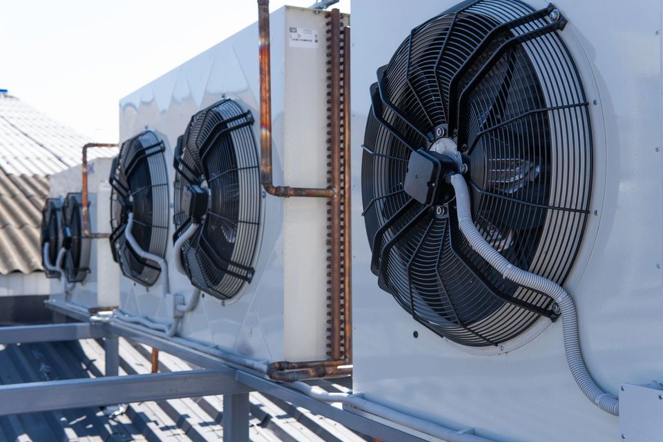 Grandi ventilatori industriali installati su unità HVAC sui tetti, esposti alla luce solare diretta.
