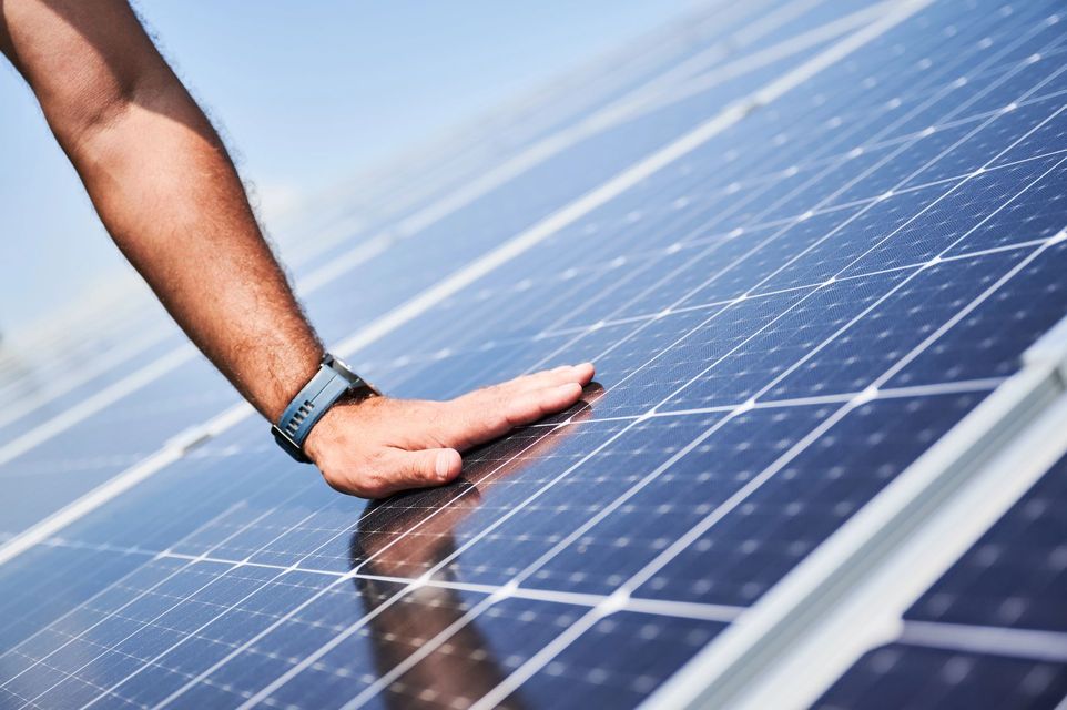 Una mano che tocca pannelli solari lucidi sotto la luce intensa del sole