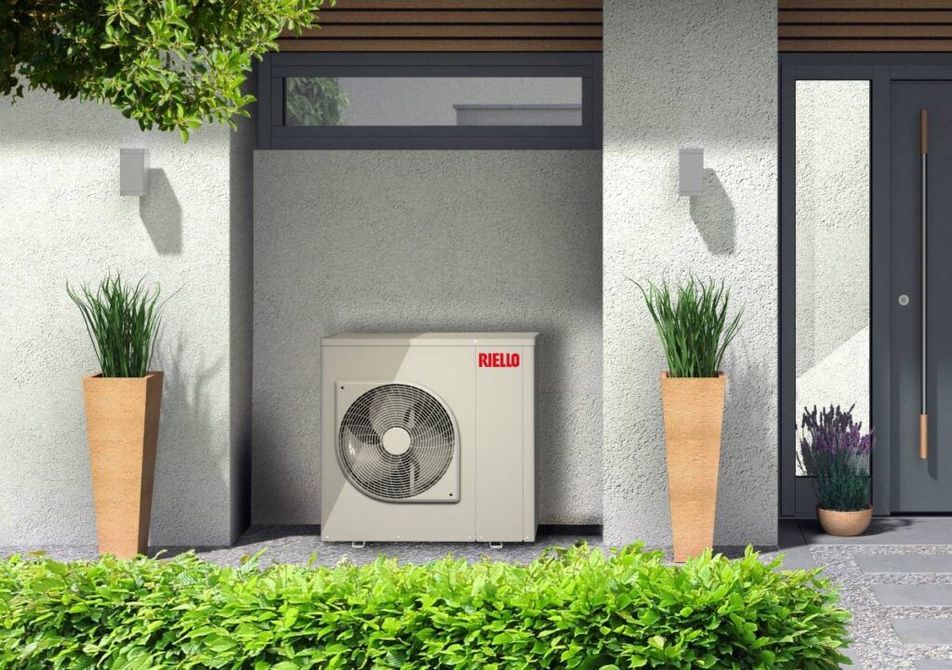 Unità esterna di climatizzazione posizionata tra vasi di piante accanto all'ingresso di una casa moderna.