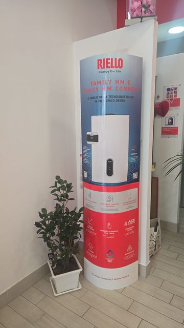 Caldaia bianca a parete con decorazione a vite e fiore rosso accanto a un termostato in uno stretto corridoio