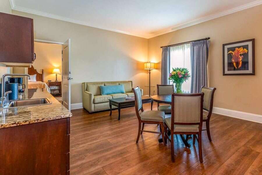 Living room and kitchenette with couch, dining table, open bedroom door, and sink area.