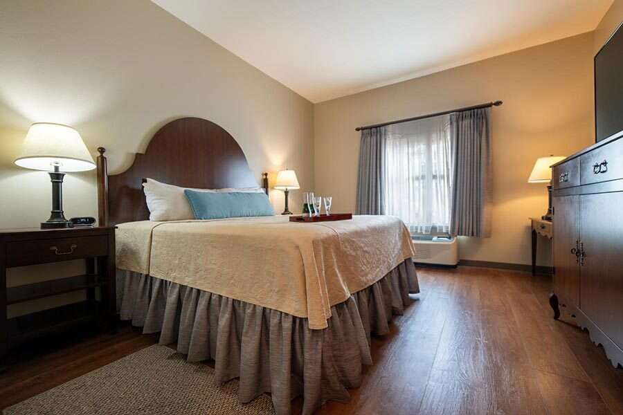 Hotel room with a bed, nightstands, and dresser. The room has warm lighting and wooden floors.