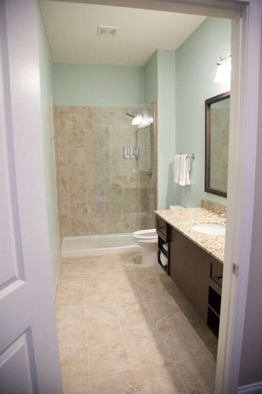 Bathroom with light green walls, beige tile floor and shower, brown vanity, and a large mirror.