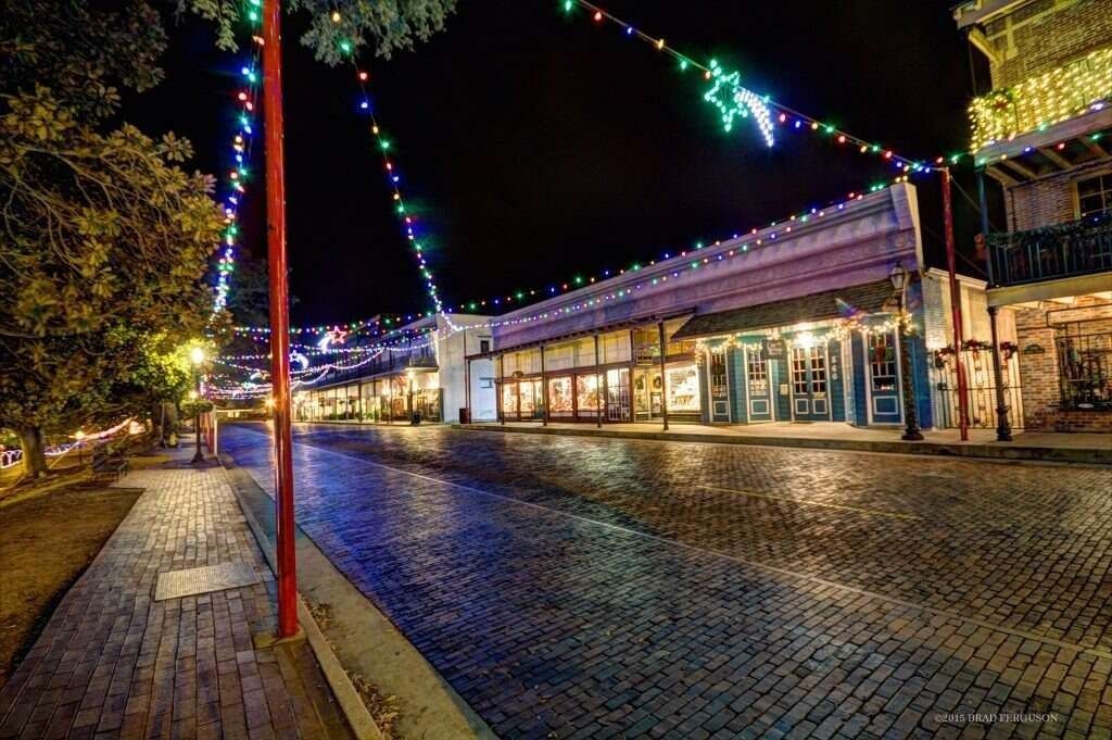 Cobblestone street at night, storefronts with Christmas lights.