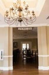 Entrance to lounge with chandelier, sign, beige walls, hardwood floor, and tables.