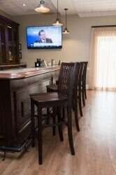 Dark wood bar with stools, TV above. Neutral walls, wood flooring.
