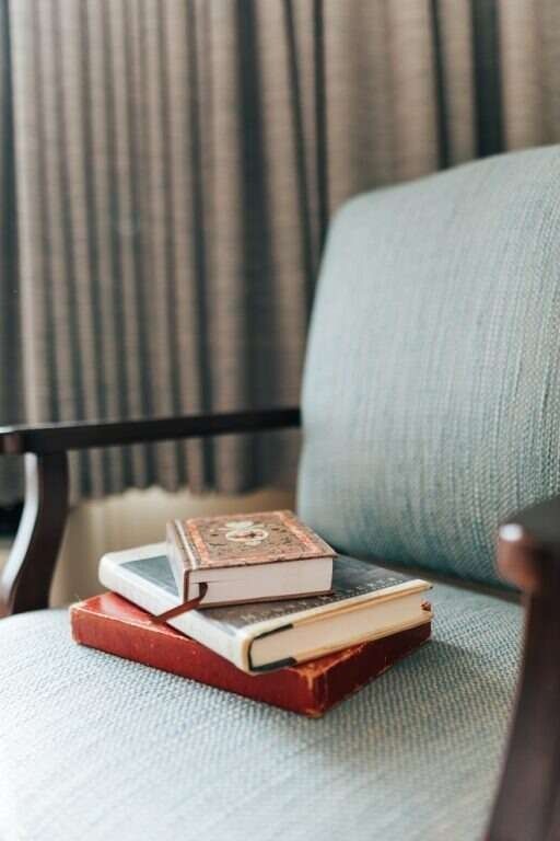 Books stacked on a teal armchair, in front of a gray curtain.
