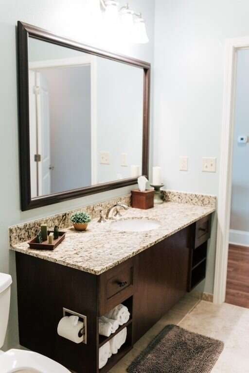Bathroom with a dark wood vanity, granite countertop, and large mirror. Towels and toilet paper are accessible.