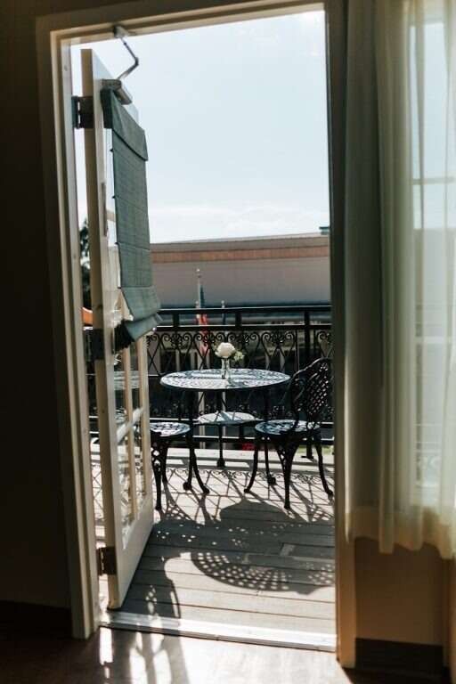 Doorway to a balcony with a round table and chairs, sunny day, with the door open, casting a shadow.