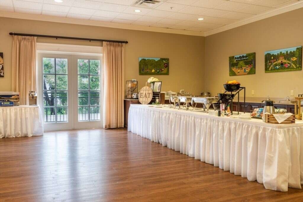 Living room with a sofa, coffee table, dining set, and window with curtains. Beige walls, hardwood floors.