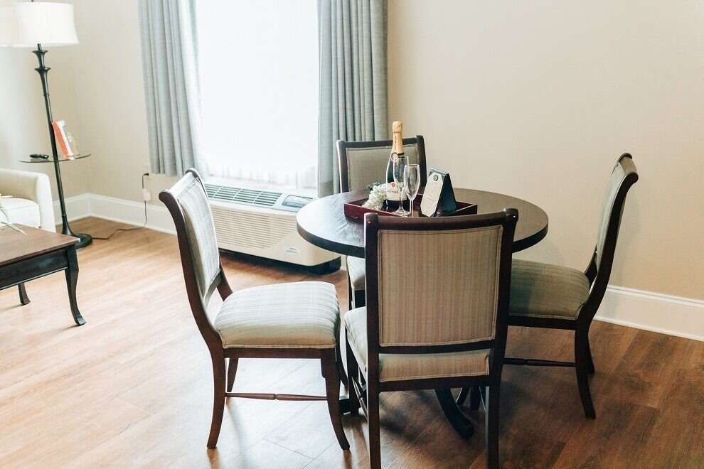 A round dining table with four chairs in a room, set with a bottle of champagne and glasses.