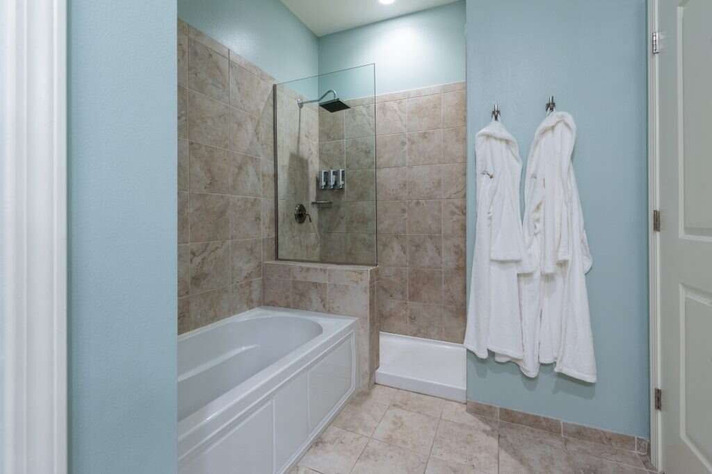 Bathroom with a bathtub, shower, blue walls, and white bathrobes hanging on hooks.