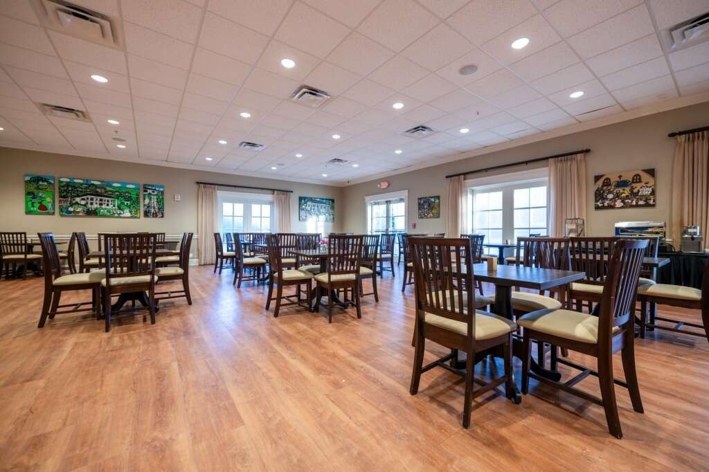 A dining room with wooden tables, chairs, and flooring. Windows, artwork, and recessed lighting.
