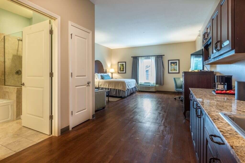Spacious studio apartment with a bed, kitchenette, and bathroom. Hardwood floors, neutral walls, and dark cabinets.
