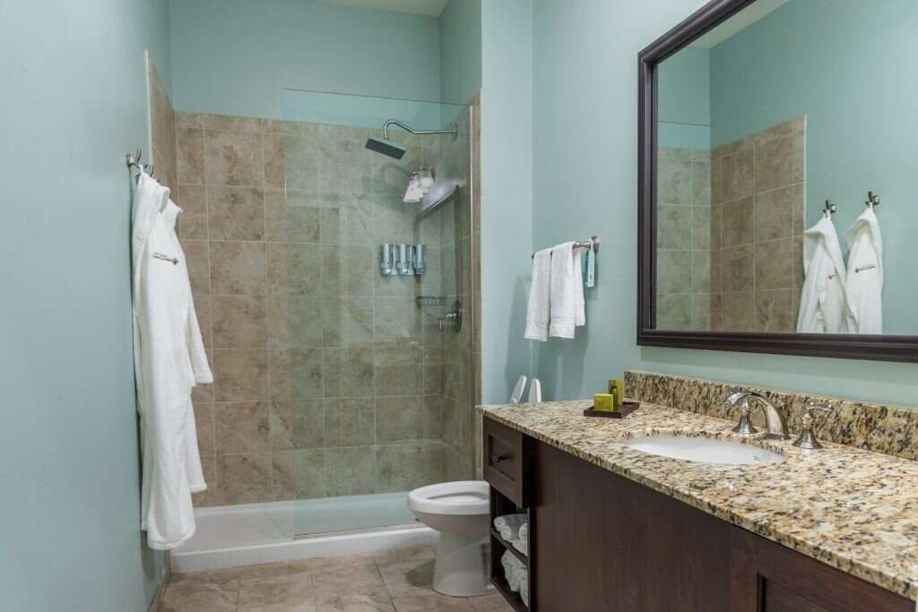 Bathroom with blue walls, brown cabinets, granite countertop, shower, and towels.