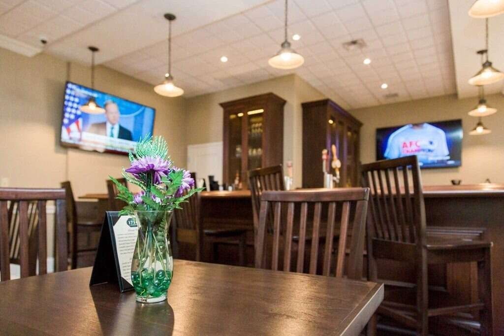 Restaurant interior: wooden tables/chairs, bar with TVs, pendant lights, flowers.